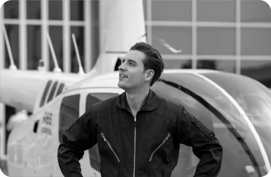 Man in flight jacket looking skyward in front of helicopter — Crosswind Culture aviation apparel